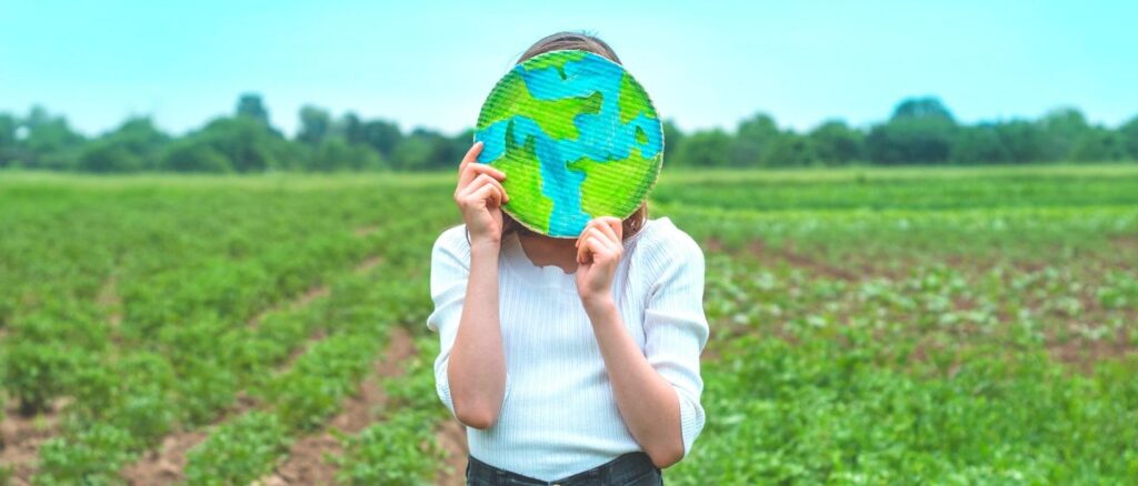 woman in field holding cardboard earth in front of face