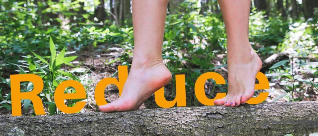 feet tiptoeing over fallen log in forest, 'reduce' written on top of log behind feet in bold orange lettering
